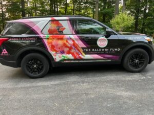 A black suv with a pink and red car wrap on the side.
