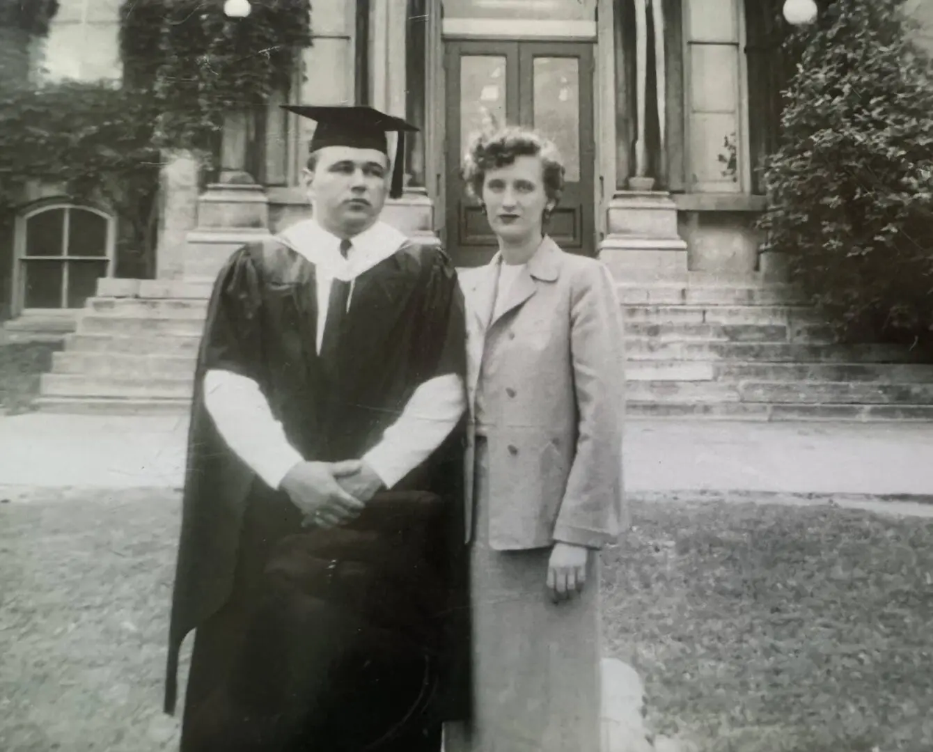 A man and woman in graduation attire standing outside.